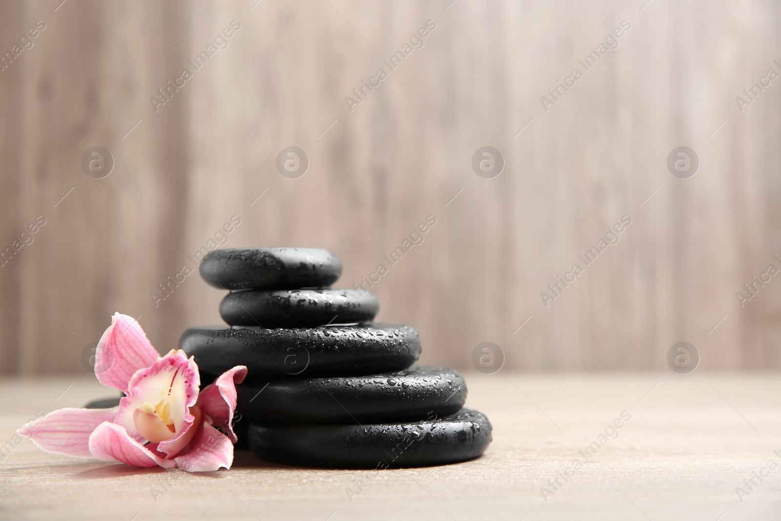 Photo of Stack of black spa stones with flower on wooden background. Space for text