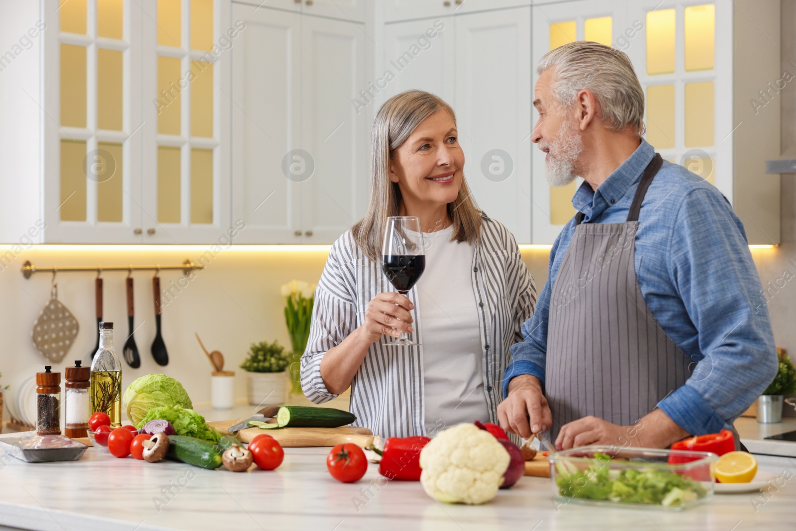 Photo of Happy senior couple cooking together in kitchen. Woman with glass of wine near her husband