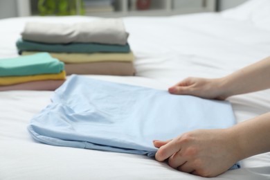 Woman folding clothes on bed indoors, closeup