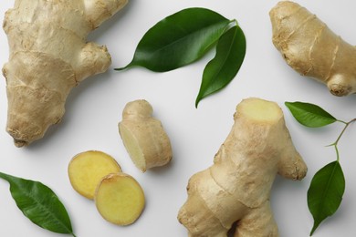 Photo of Fresh ginger with green leaves on white background, flat lay