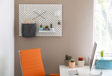 Photo of Modern workplace and pegboard with different cacti in room