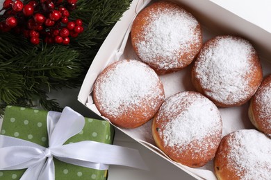 Photo of Delicious sweet buns in box, decorative branches and gift on table, flat lay