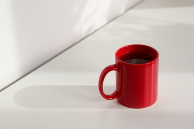 Photo of Red ceramic mug with drink on white table indoors. Mockup for design