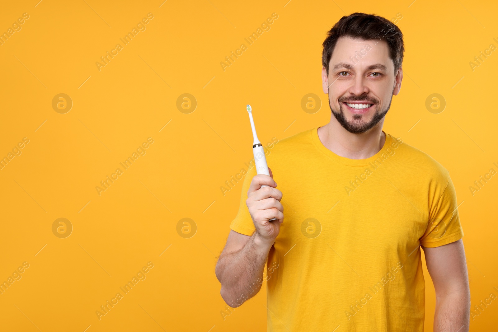 Photo of Happy man holding electric toothbrush on yellow background. Space for text