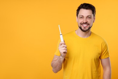 Happy man holding electric toothbrush on yellow background. Space for text