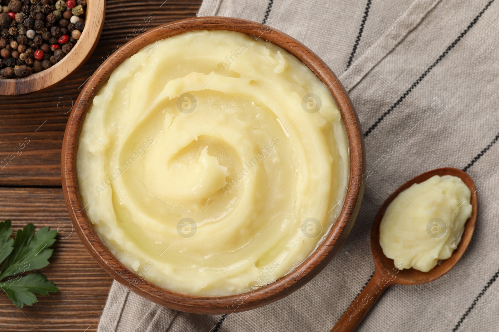 Photo of Bowl of tasty mashed potato, parsley and pepper on wooden table, flat lay