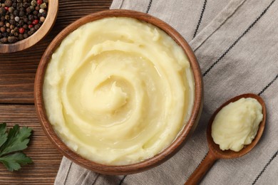 Bowl of tasty mashed potato, parsley and pepper on wooden table, flat lay