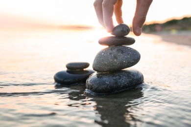 Photo of Woman stacking dark stones on sand near sea, space for text. Zen concept