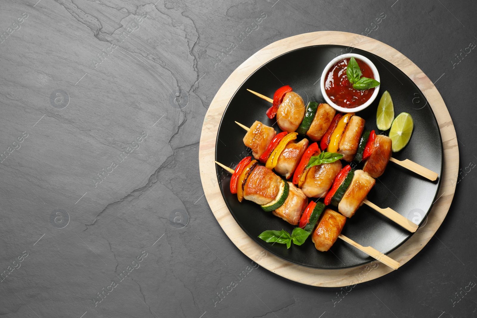 Photo of Delicious chicken shish kebabs with vegetables and sauce on grey table, top view. Space for text