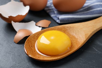 Photo of Wooden spoon with raw egg yolk on black table, closeup