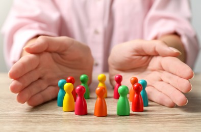 Woman protecting colorful pawns at wooden table, closeup. Social inclusion concept