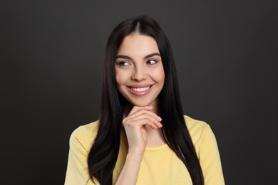 Photo of Portrait of happy young woman with beautiful black hair and charming smile on dark background