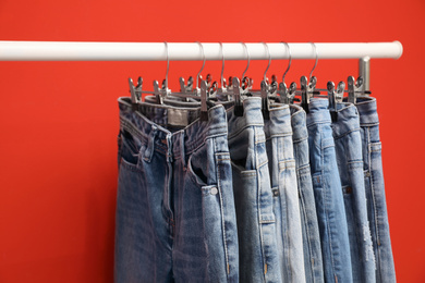 Photo of Rack with stylish jeans on red background, closeup