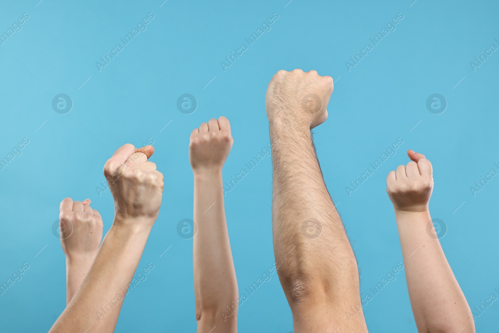 Photo of Strike. People showing clenched fists on light blue background, closeup