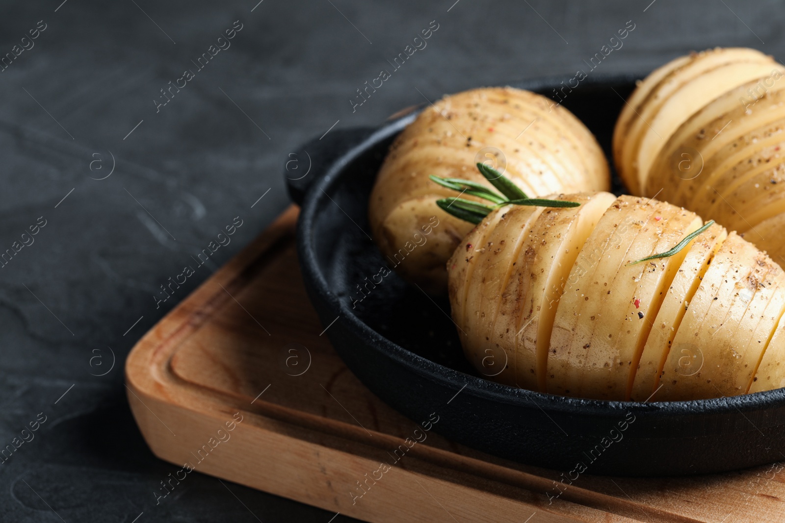 Photo of Raw Hasselback potatoes with rosemary in baking pan on dark grey table, closeup. Space for text