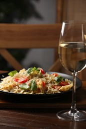 Photo of Plate of delicious pasta with tomatoes, basil and glass at wooden table