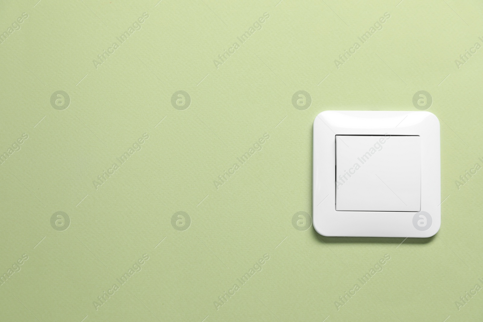Photo of Modern plastic light switch on green background. Space for text