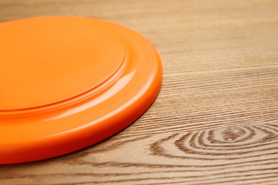 Orange plastic frisbee disk on wooden background, closeup. Space for text