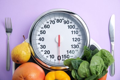 Photo of Scales, healthy food and cutlery on violet background, flat lay