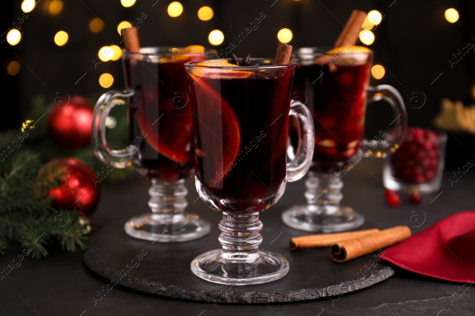 Photo of Aromatic mulled wine on black table against blurred festive lights