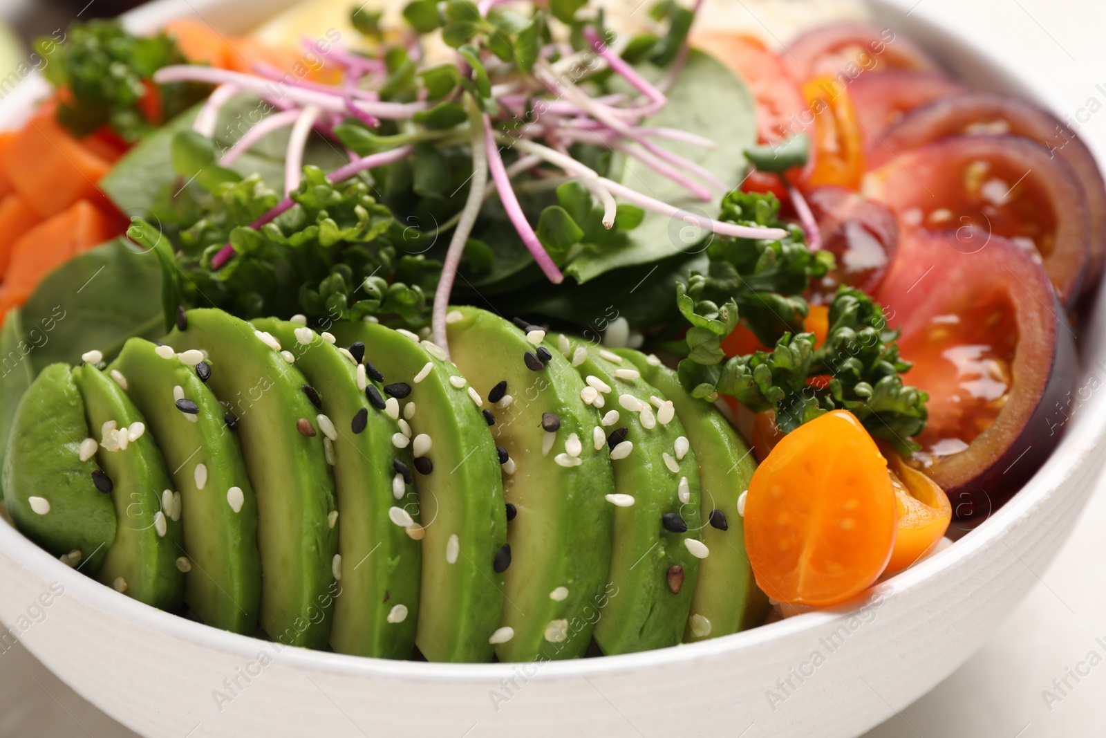 Photo of Delicious vegan bowl with avocados, microgreens and tomatoes on grey table, closeup