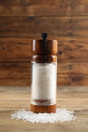 Shaker with salt on wooden table, closeup