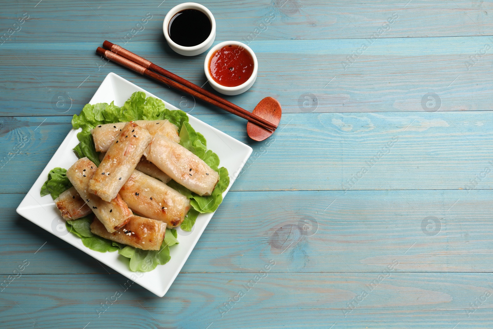 Photo of Tasty fried spring rolls, lettuce and sauces on light blue wooden table, flat lay. Space for text