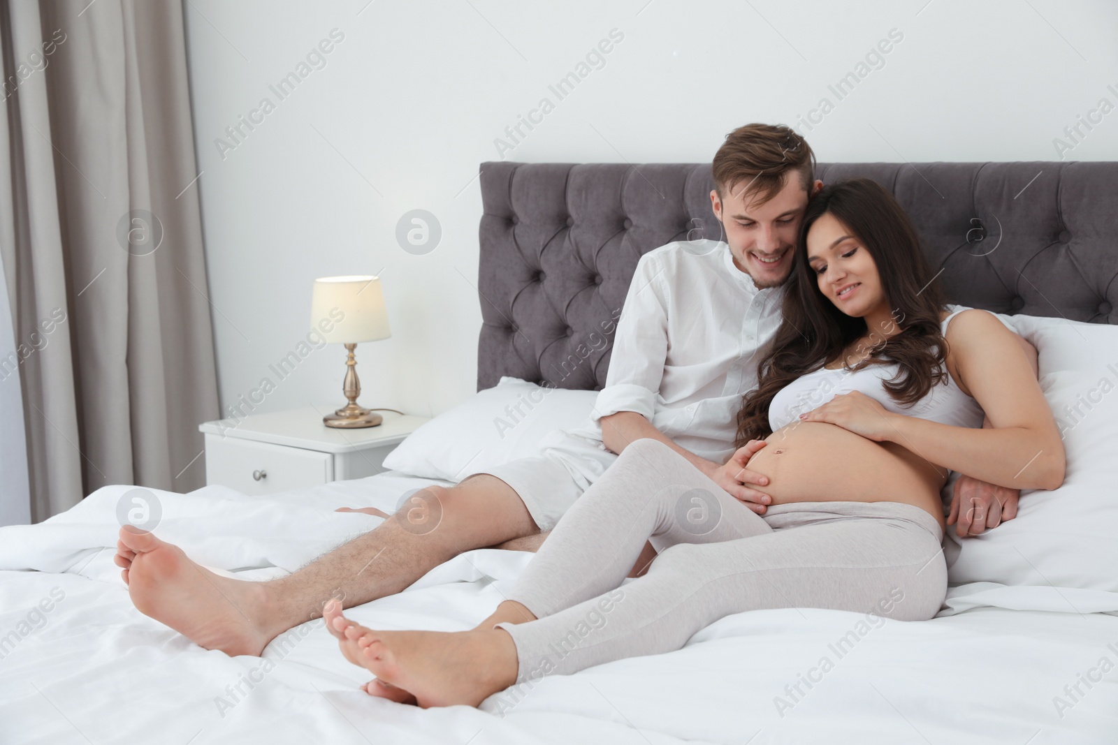 Photo of Young husband and his pregnant wife lying in bed at home