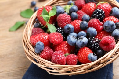 Photo of Many different fresh ripe berries in wicker basket on wooden table, closeup