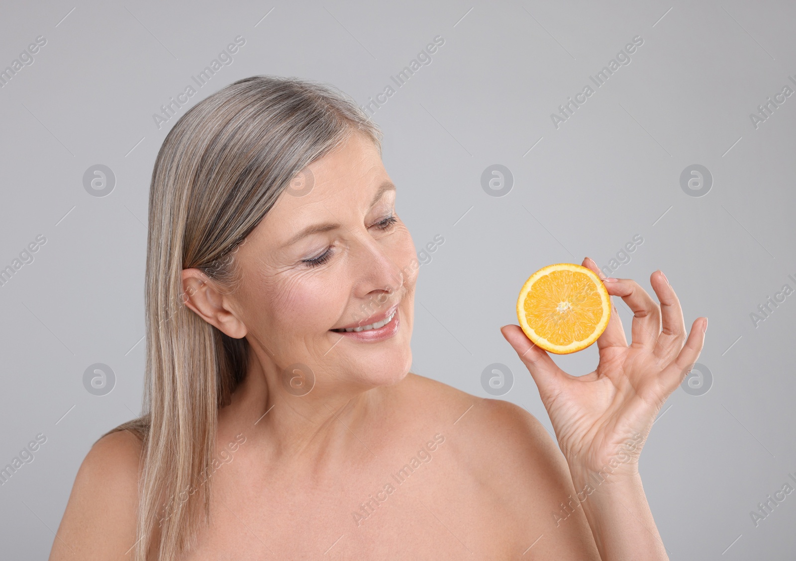 Photo of Beautiful woman with half of orange rich in vitamin C on grey background