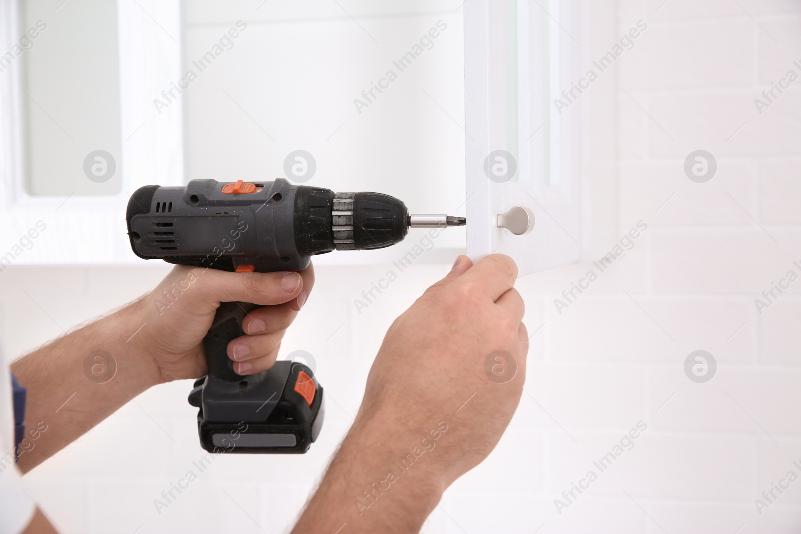 Photo of Worker installing handle on cabinet door with screw gun in kitchen, closeup