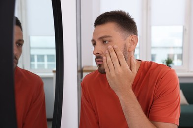 Photo of Sleep deprived man looking at himself in mirror indoors