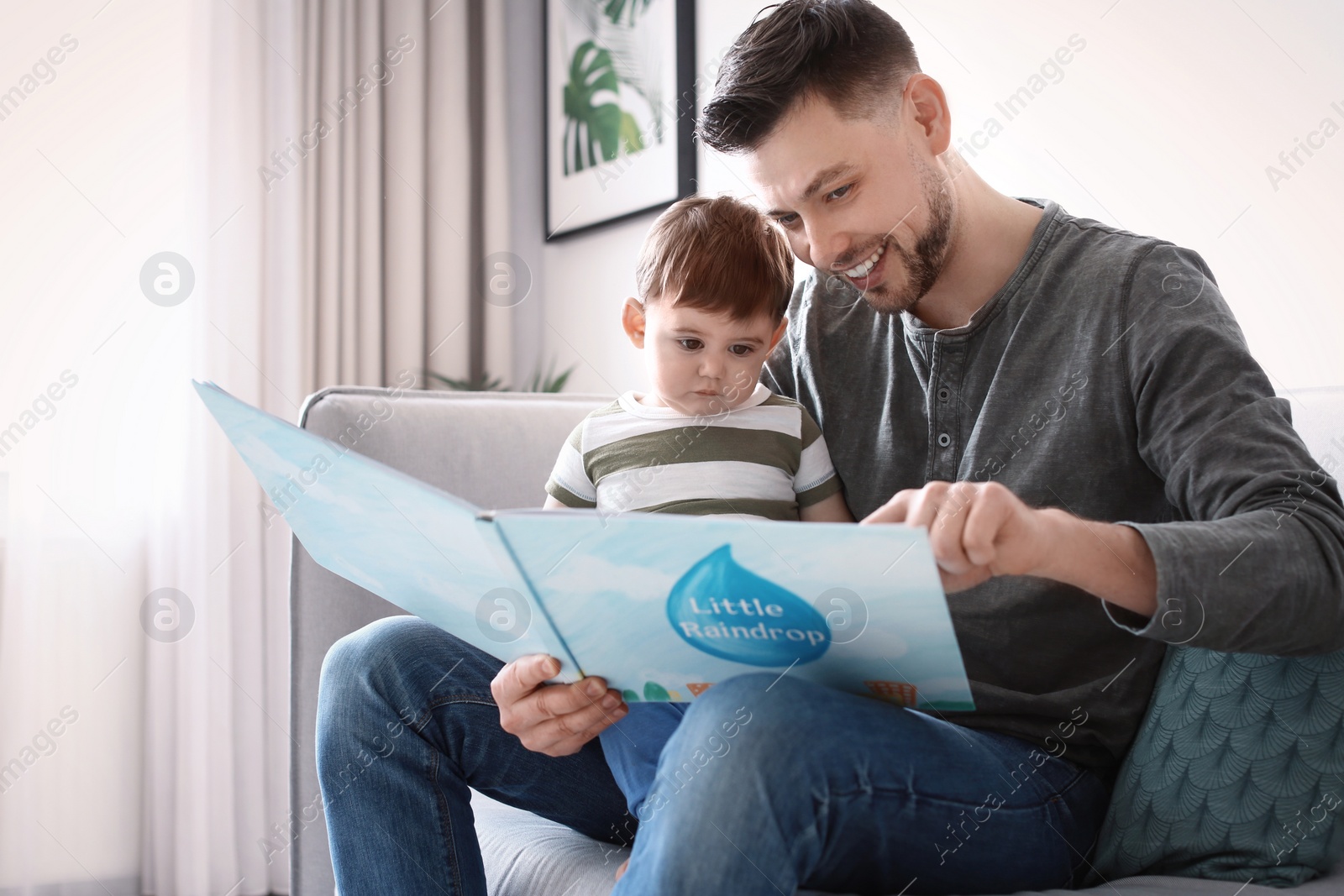 Photo of Dad and his son reading book on sofa at home