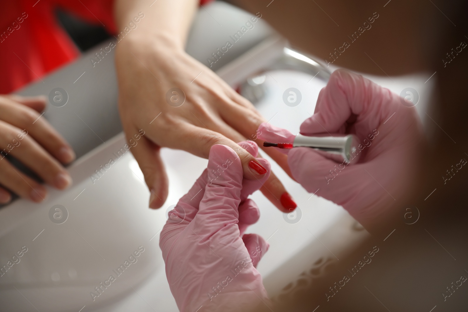 Photo of Professional manicurist applying polish on client's nails in beauty salon, closeup