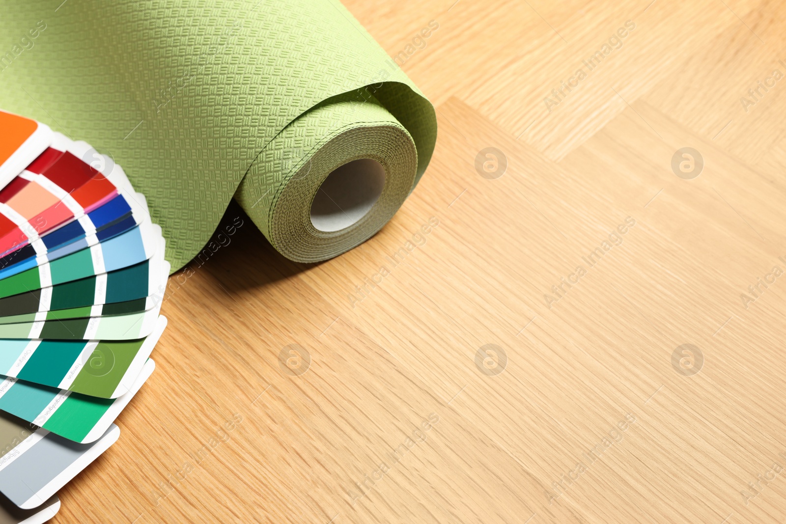 Photo of Green wallpaper roll and color palette samples on wooden table, space for text