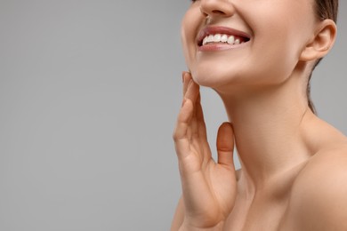 Smiling woman touching her chin on grey background, closeup. Space for text