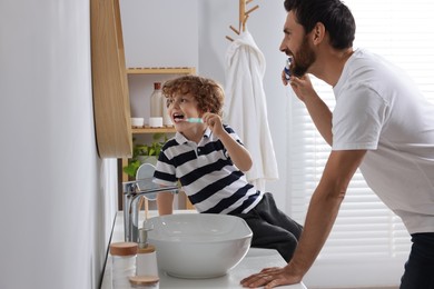 Father and his son brushing teeth together in bathroom