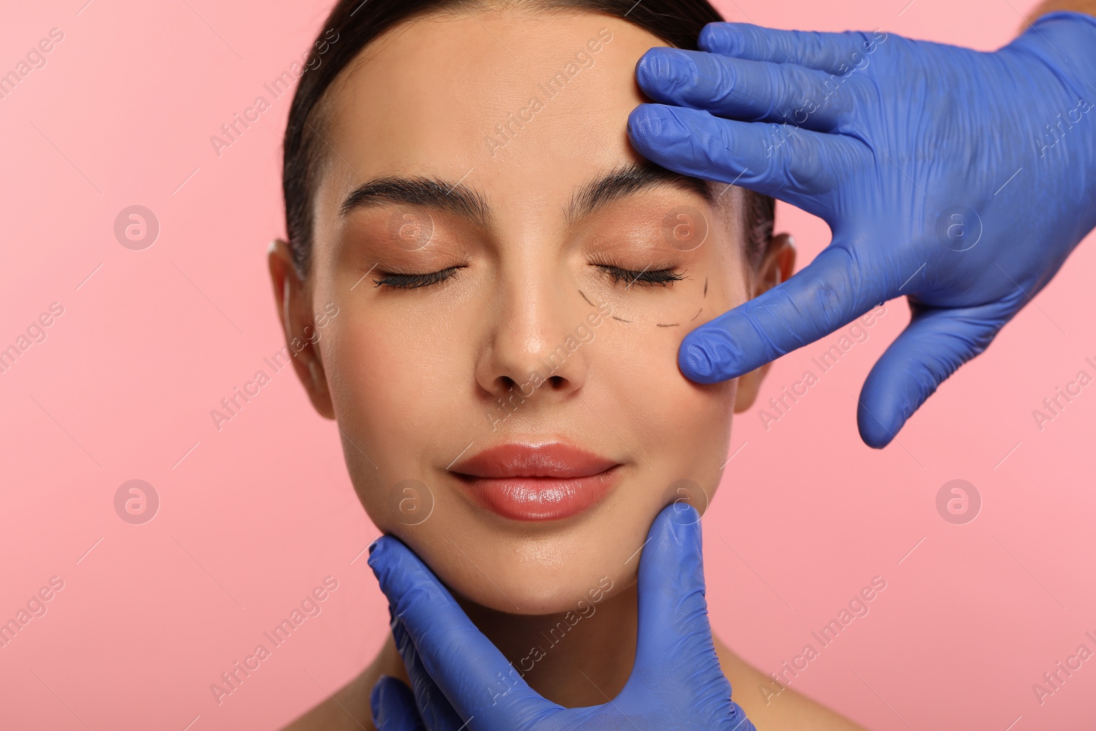 Photo of Doctor checking patient's face before cosmetic surgery operation on pink background, closeup