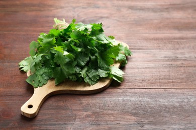 Photo of Fresh green coriander leaves on wooden table, space for text