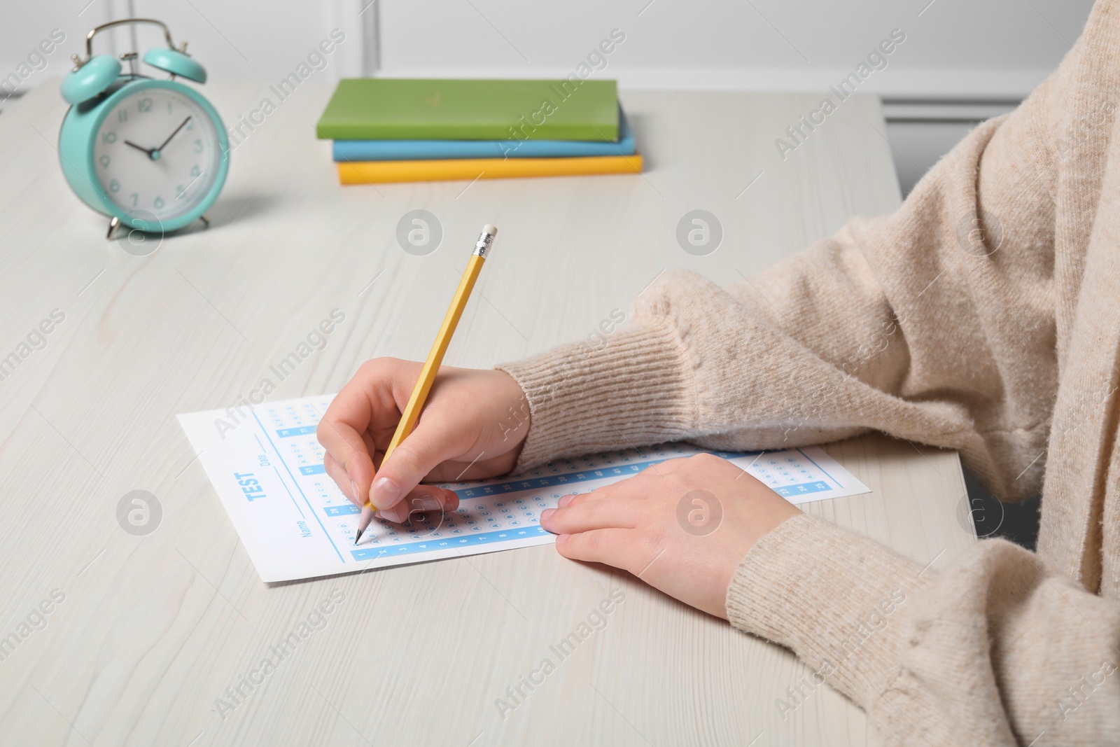 Photo of Student filling answer sheet at white wooden table, closeup. Passing exam