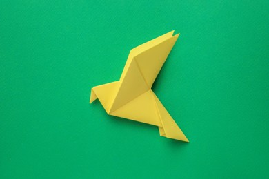 Photo of Beautiful yellow origami bird on green background, top view