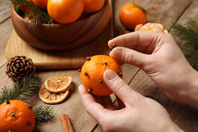 Woman decorating fresh tangerine with cloves at wooden table, closeup. Christmas atmosphere