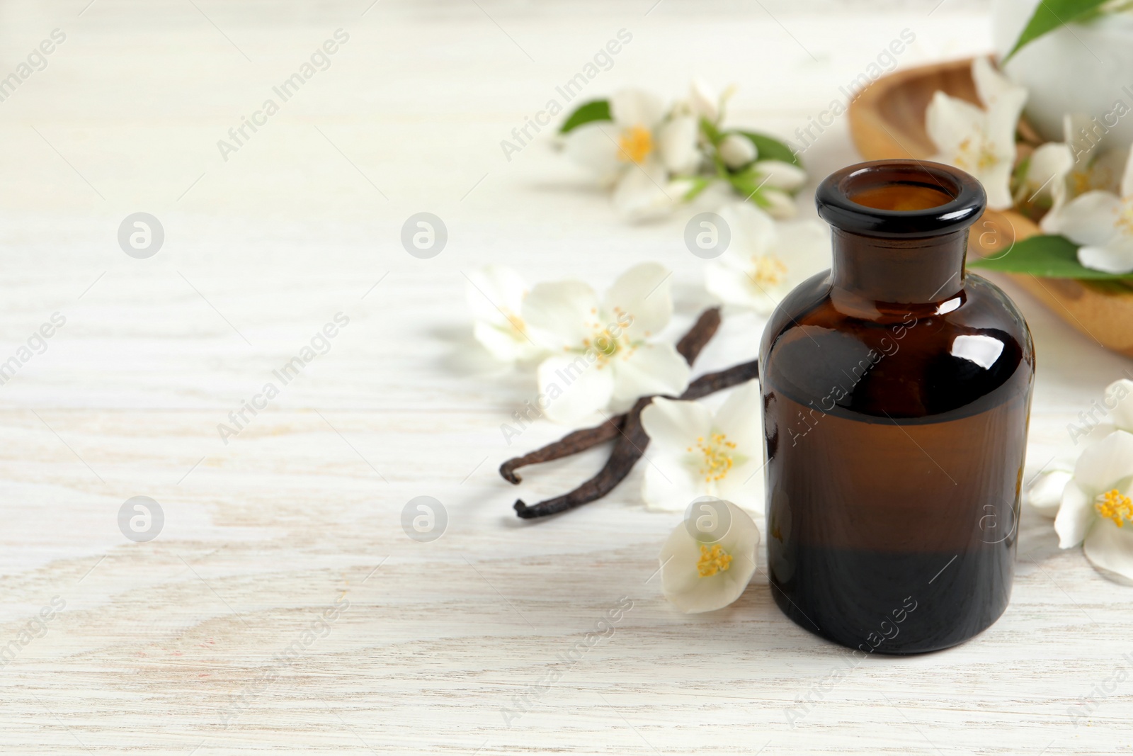 Photo of Jasmine essential oil and fresh flowers on white wooden table, space for text