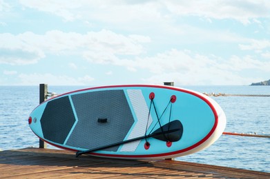 Photo of SUP board with paddle on wooden pier near sea