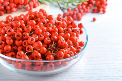 Photo of Fresh ripe rowan berries in glass bowl on white wooden table, closeup