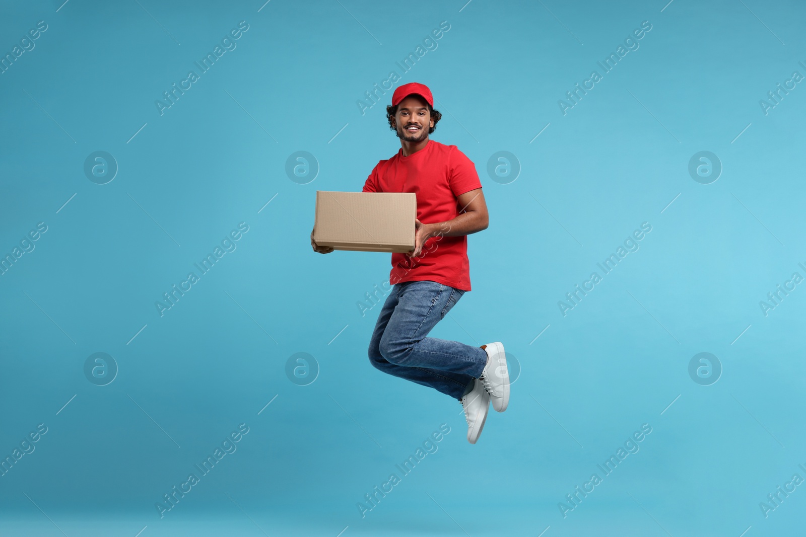 Photo of Happy young courier with parcel jumping on light blue background
