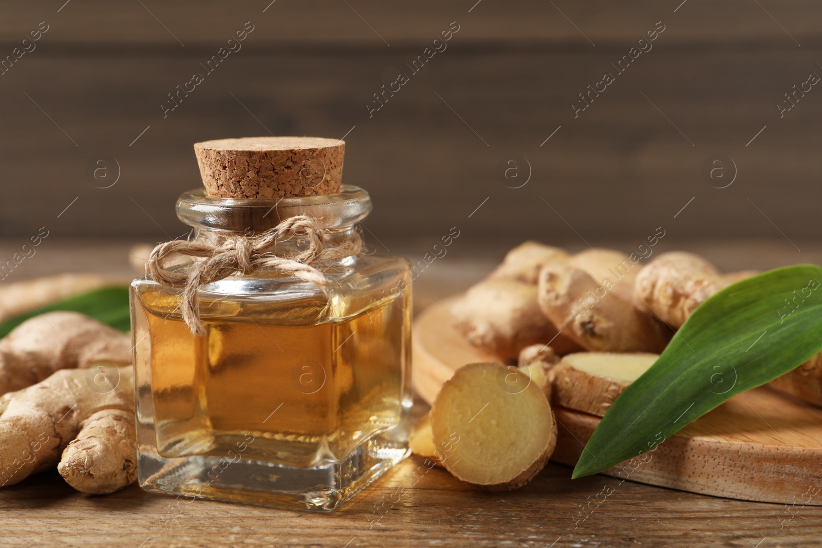 Photo of Glass bottle of essential oil and ginger root on wooden table