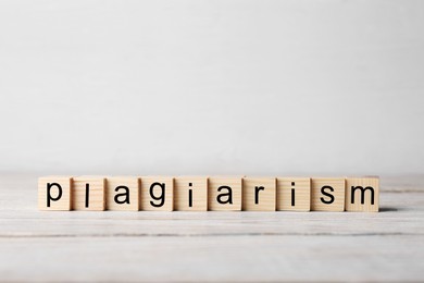 Photo of Wooden cubes with word Plagiarism on white table, space for text