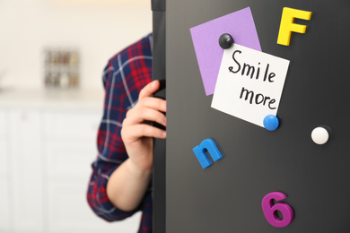 Photo of Woman opening refrigerator door with SMILE MORE note indoors, closeup