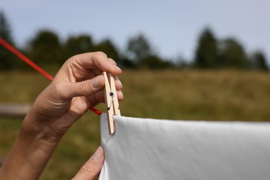 Photo of Woman hanging clean laundry with clothespin on washing line outdoors, closeup